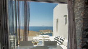 Un coin repas avec une table dressée pour deux personnes, une vue sur la mer et un mur en pierre.