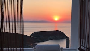 Une chambre avec vue sur le coucher de soleil sur la mer, un lit, une table de chevet et une lampe.