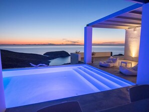Un espace extérieur moderne, aménagé pour se détendre, avec vue sur la mer au coucher du soleil.