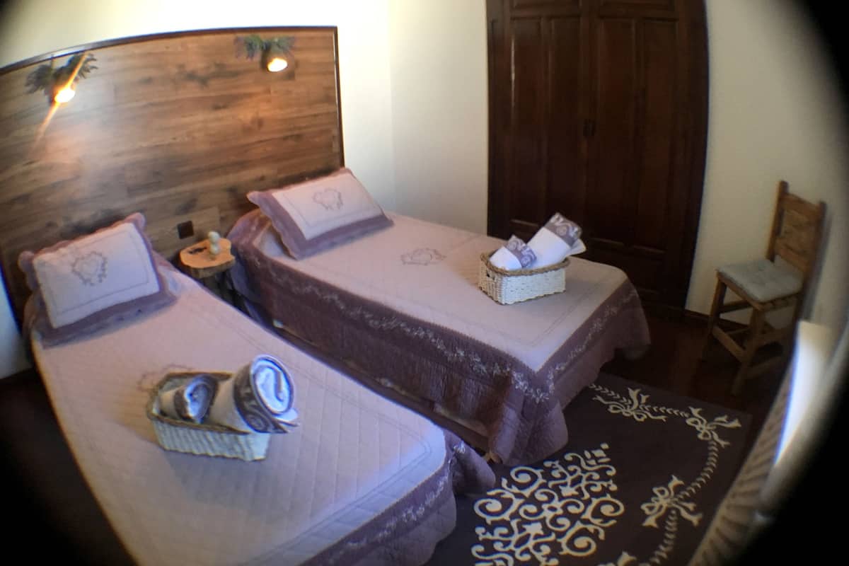 Ein Zimmer mit zwei Betten, jedes mit einem Kissen und einem Korb. Im Zimmer befindet sich ein Holzschrank und ein Stuhl.
