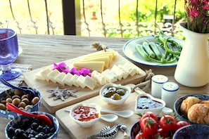 Una mesa de madera con diversos alimentos como queso, aceitunas, tomates y pan.