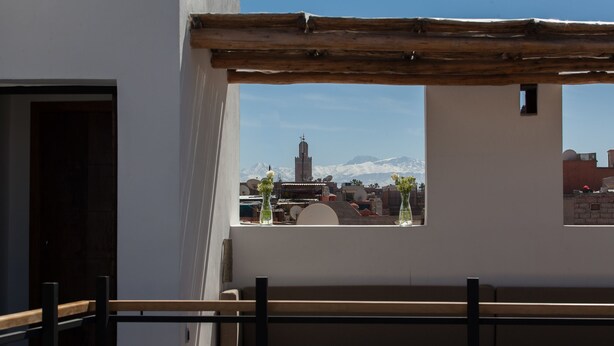 Ein Balkon mit Holzgeländer, Blick auf ein Gebirge und ein Gebäude mit einem Glockenturm.