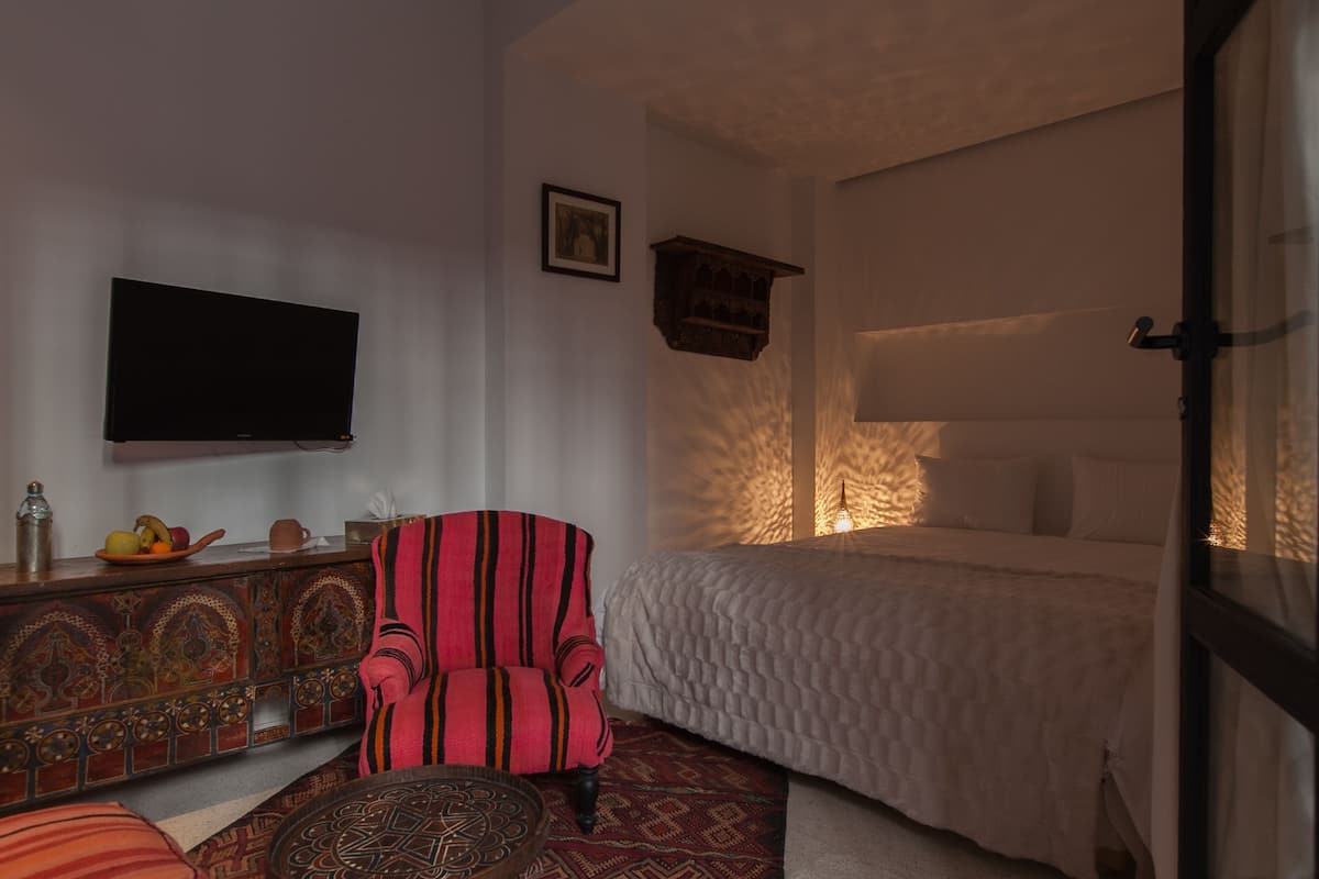 A bedroom with a bed, a television on the wall, a chair, and a decorative cabinet.