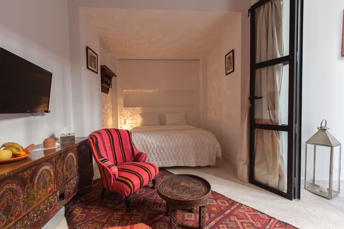 A bedroom with a bed, a television, a red chair, a small table, and a decorative lantern.