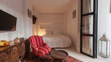 A bedroom with a bed, a television, a red chair, a small table, and a decorative lantern.