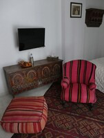 A room with a television mounted on the wall, a decorative cabinet with intricate designs, a striped armchair, and a patterned rug.