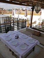 Un área de comedor en la azotea con una mesa dispuesta para seis personas, rodeada por una valla de madera y plantas en macetas.