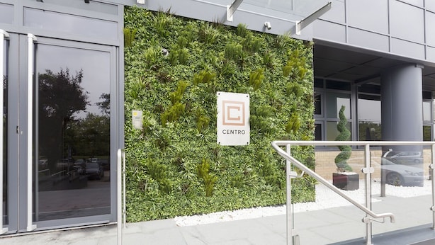 L'ingresso di un edificio con un giardino verticale verde, un cartello Centro e una scala in metallo che conduce all'interno.