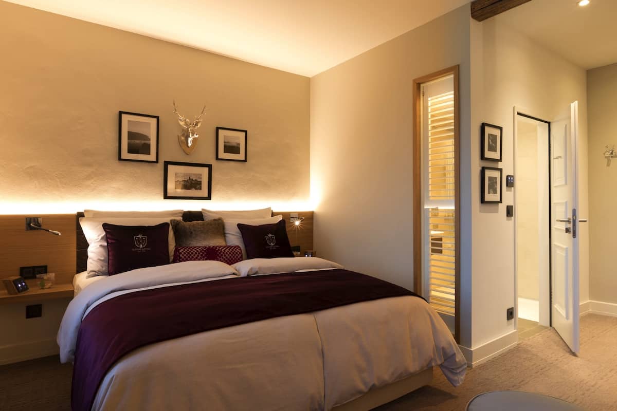 A hotel room with a large bed, a wooden headboard, a wall-mounted deer head decoration, and framed pictures.