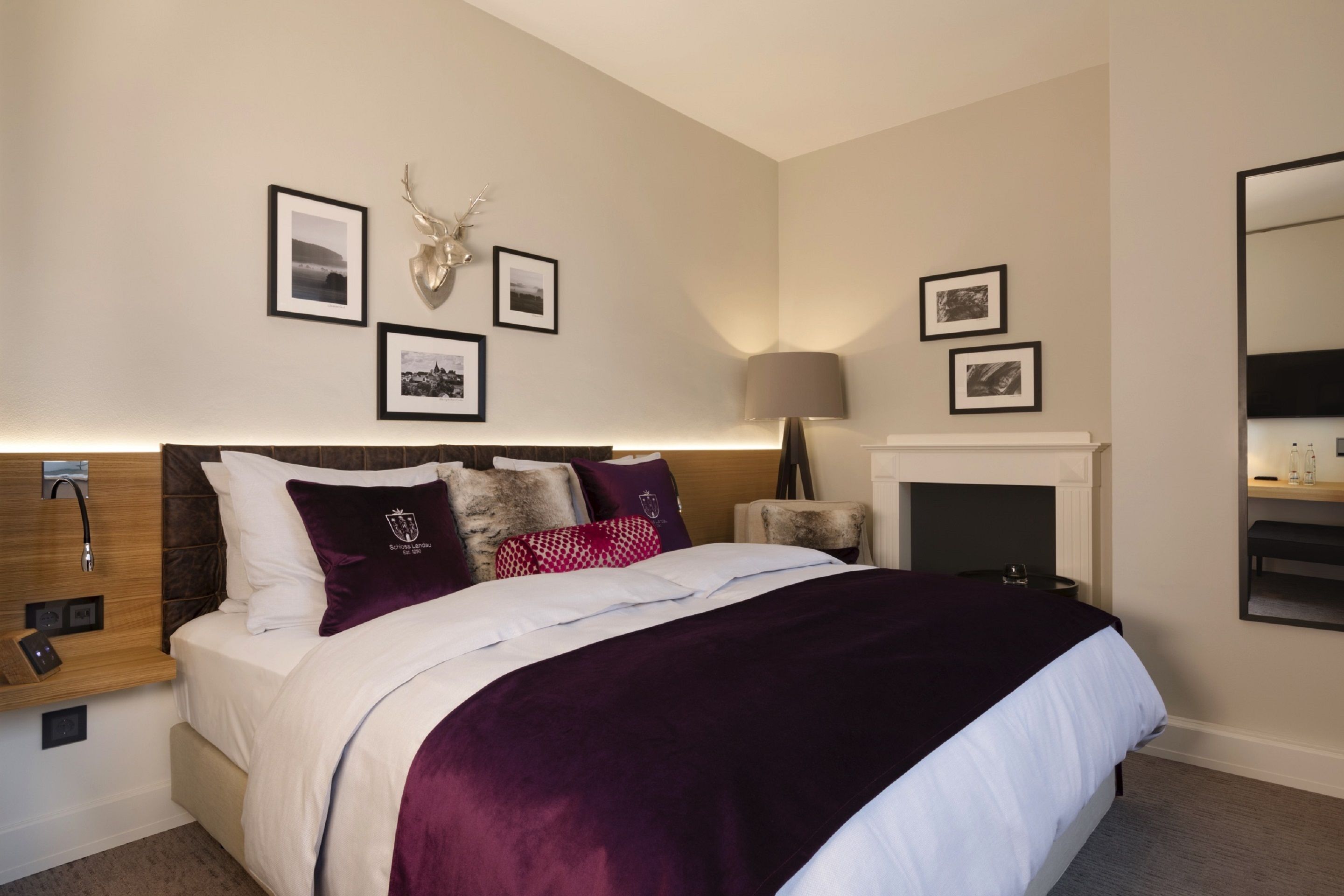 Une chambre à coucher moderne avec un grand lit, une tête de lit en bois, une cheminée et des tableaux encadrés accrochés aux murs.
