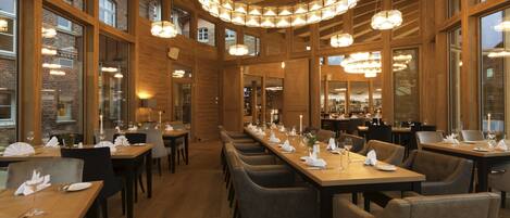 Un restaurante con interiores de madera, varias mesas de comedor y candelabros colgantes.