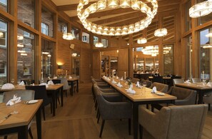 A restaurant with wooden interiors, multiple dining tables, and hanging chandeliers. - Hotel Brunnenhaus Schloss Landau (Bad Arolsen)