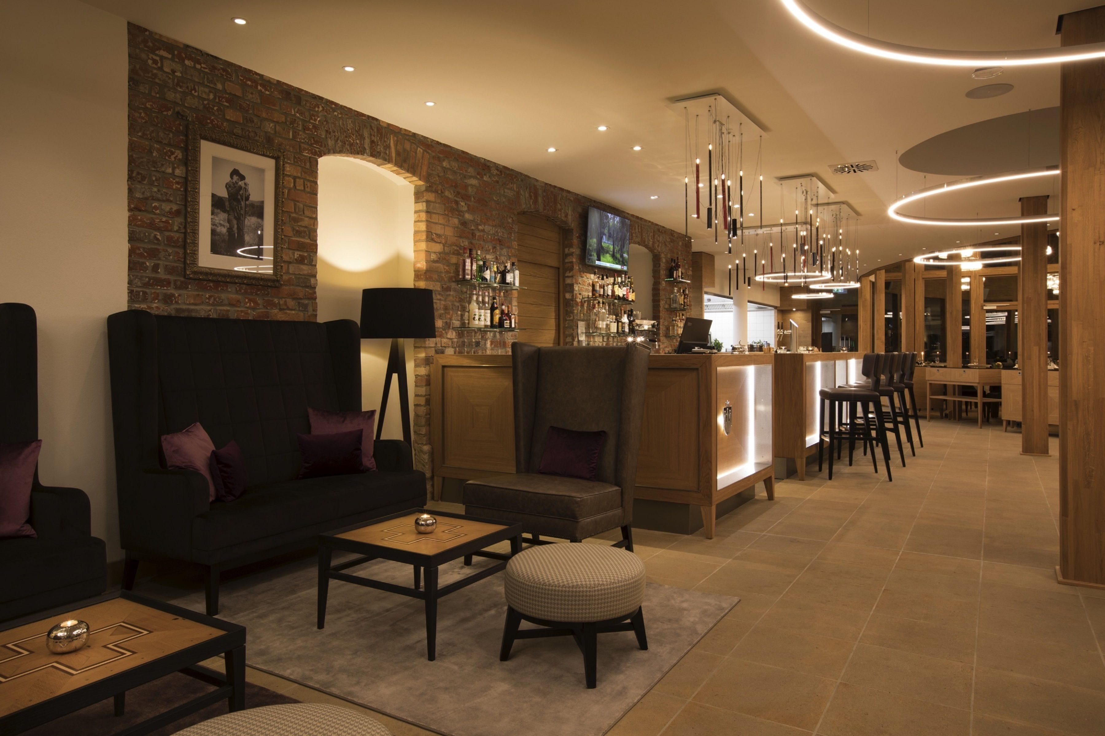 A modern lounge area with a brick wall, a bar, and seating arrangements including a sofa, armchairs, and ottomans.