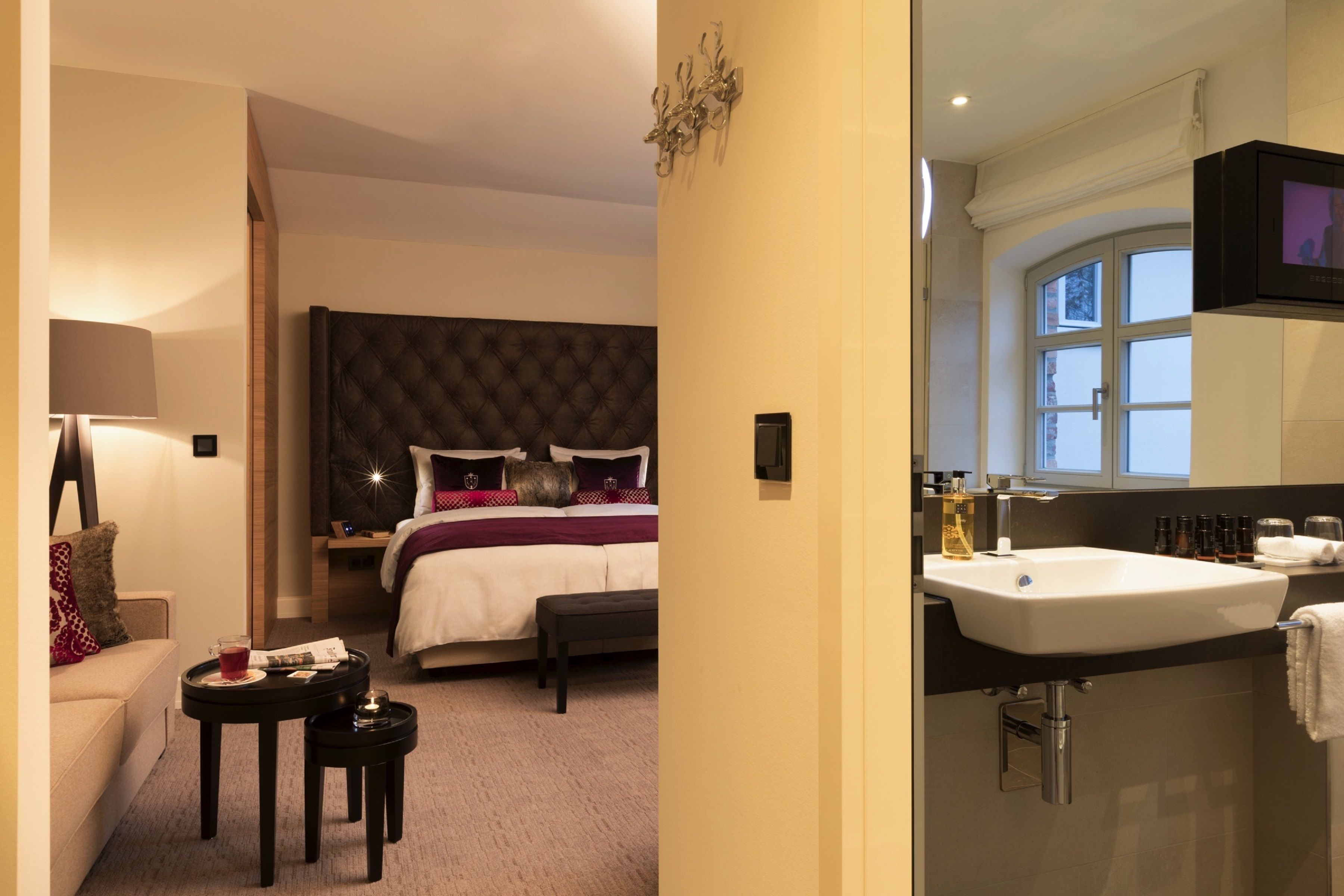 Hotelkamer met een bed, nachtkastje, lamp en een badkamer met wastafel en spiegel.