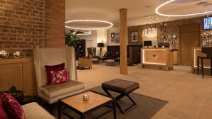 A hotel lobby with a brick wall, a reception desk, seating area, and a bar. - Hotel Brunnenhaus Schloss Landau (Bad Arolsen)