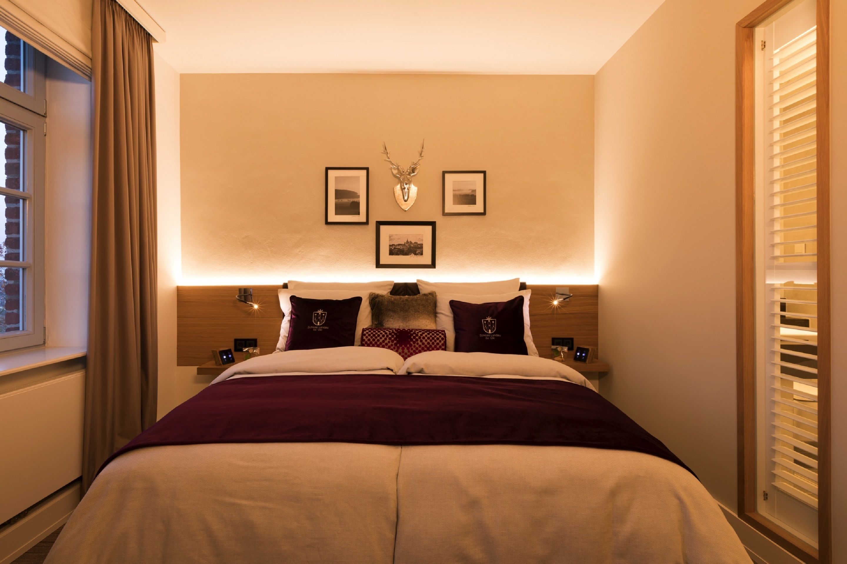 Ein Hotelzimmer mit einem großen Bett, einem Kopfteil mit einem aufgehängten Hirsch und gerahmten Bildern an der Wand.