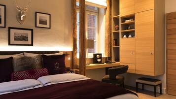 Ein Hotelzimmer mit einem großen Bett, einem Schreibtisch, einem Sessel, einem Bücherregal und gerahmten Bildern an der Wand.