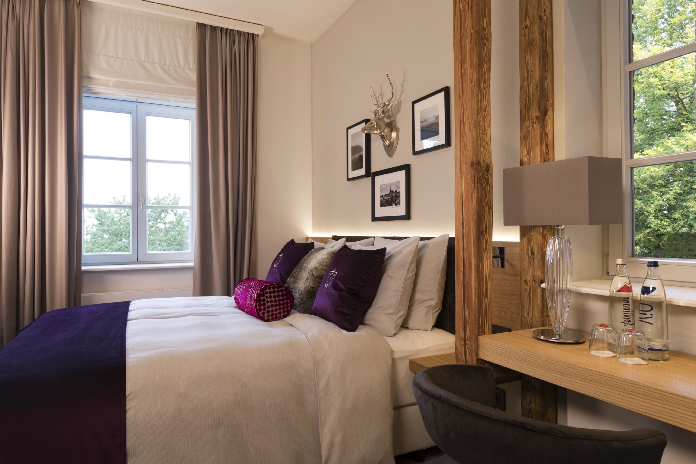 A hotel room with a bed, a desk, a chair, a window with curtains, and wall-mounted pictures.