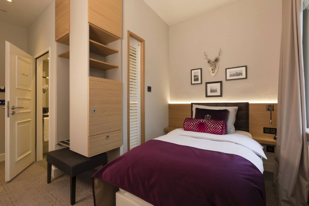 A bedroom with a bed, a wooden wardrobe, a bench, and a wall-mounted deer head decoration.