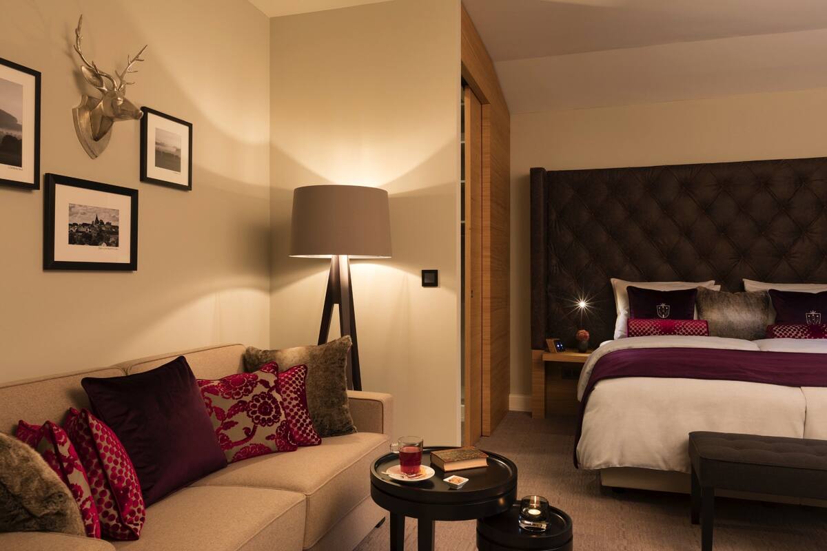 A hotel room with a bed, a sofa, a lamp, and framed pictures on the wall.