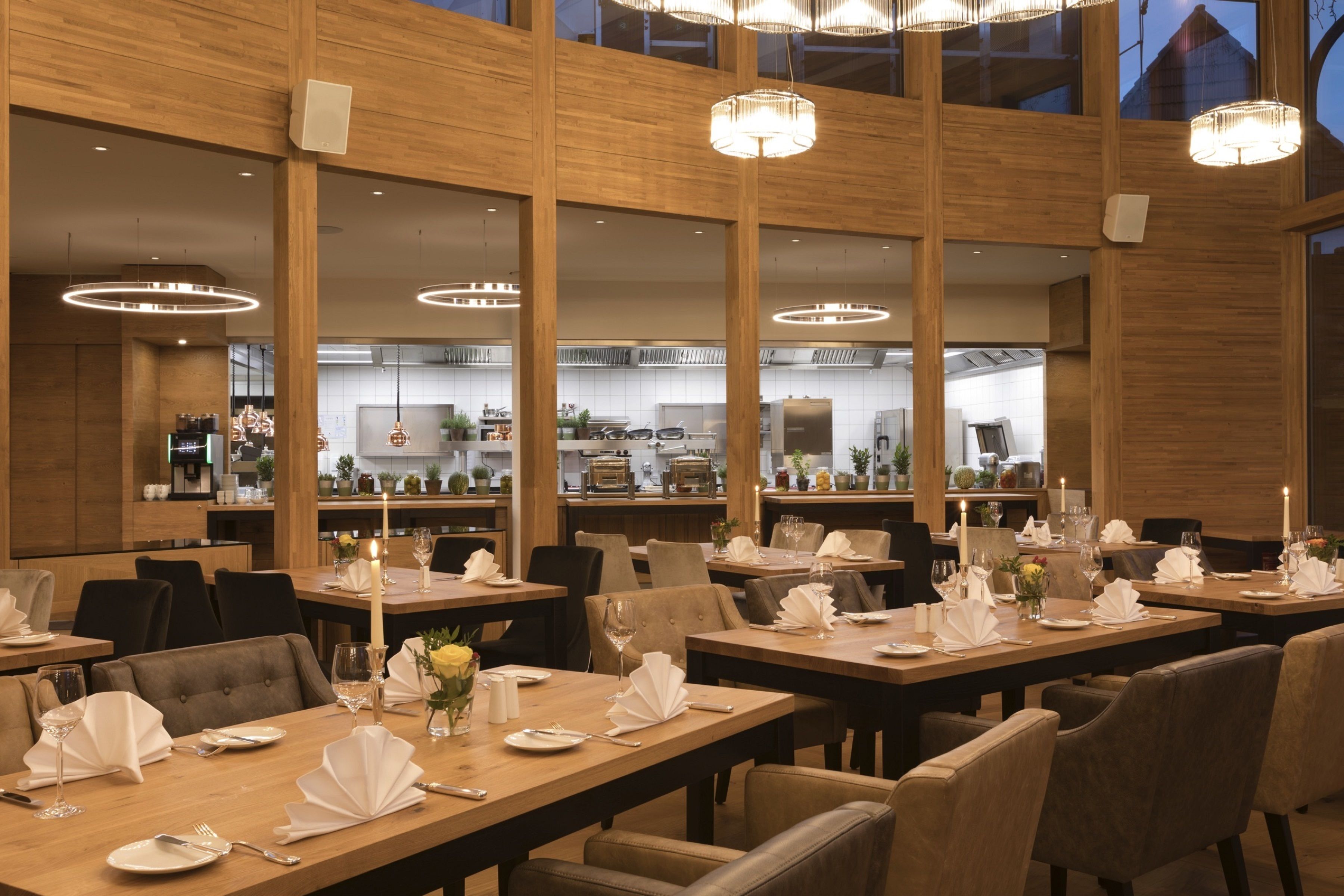 A restaurant with multiple dining tables set for service, wooden paneling, and pendant lighting.