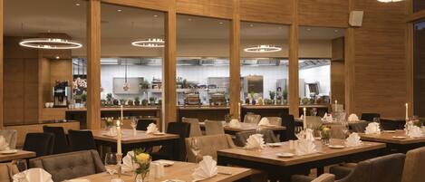 A restaurant with multiple dining tables set for service, wooden paneling, and pendant lighting.