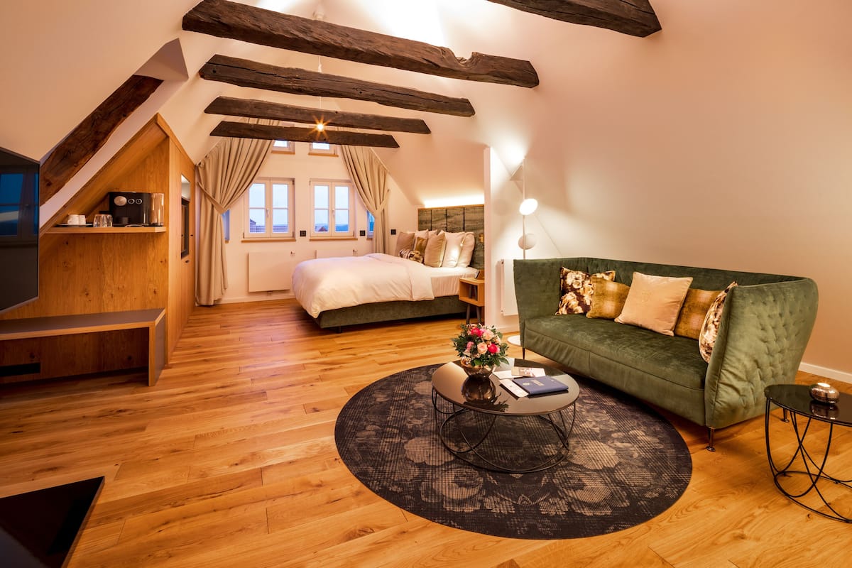 A cozy room with a wooden floor, a green sofa, a bed with white bedding, and a small table with a vase of flowers.