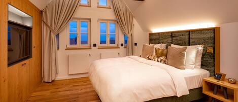 A bedroom with a large bed, wooden floor, and a headboard with a built-in clock.