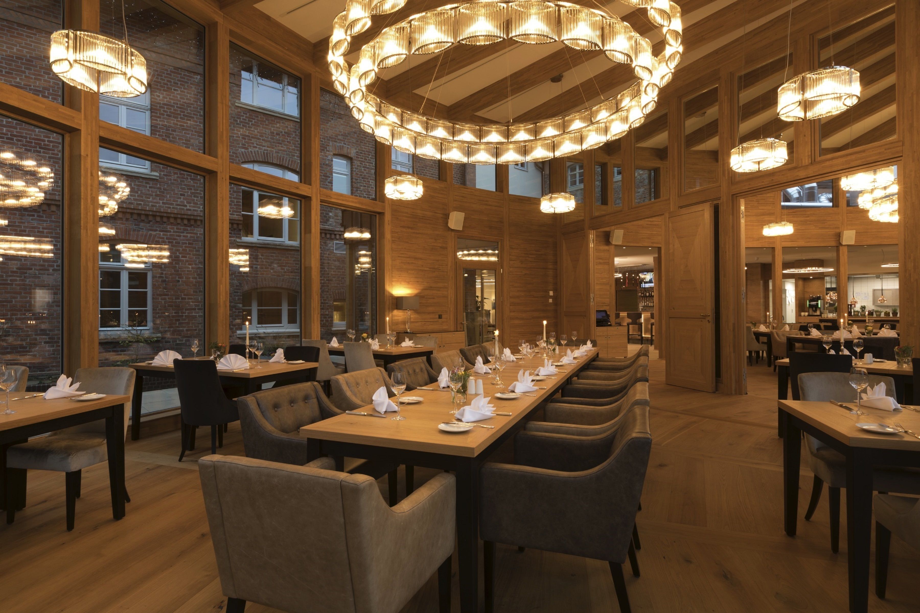 Une salle à manger spacieuse, avec de longues tables disposées pour accueillir de nombreux convives, de grandes fenêtres et des lustres modernes.