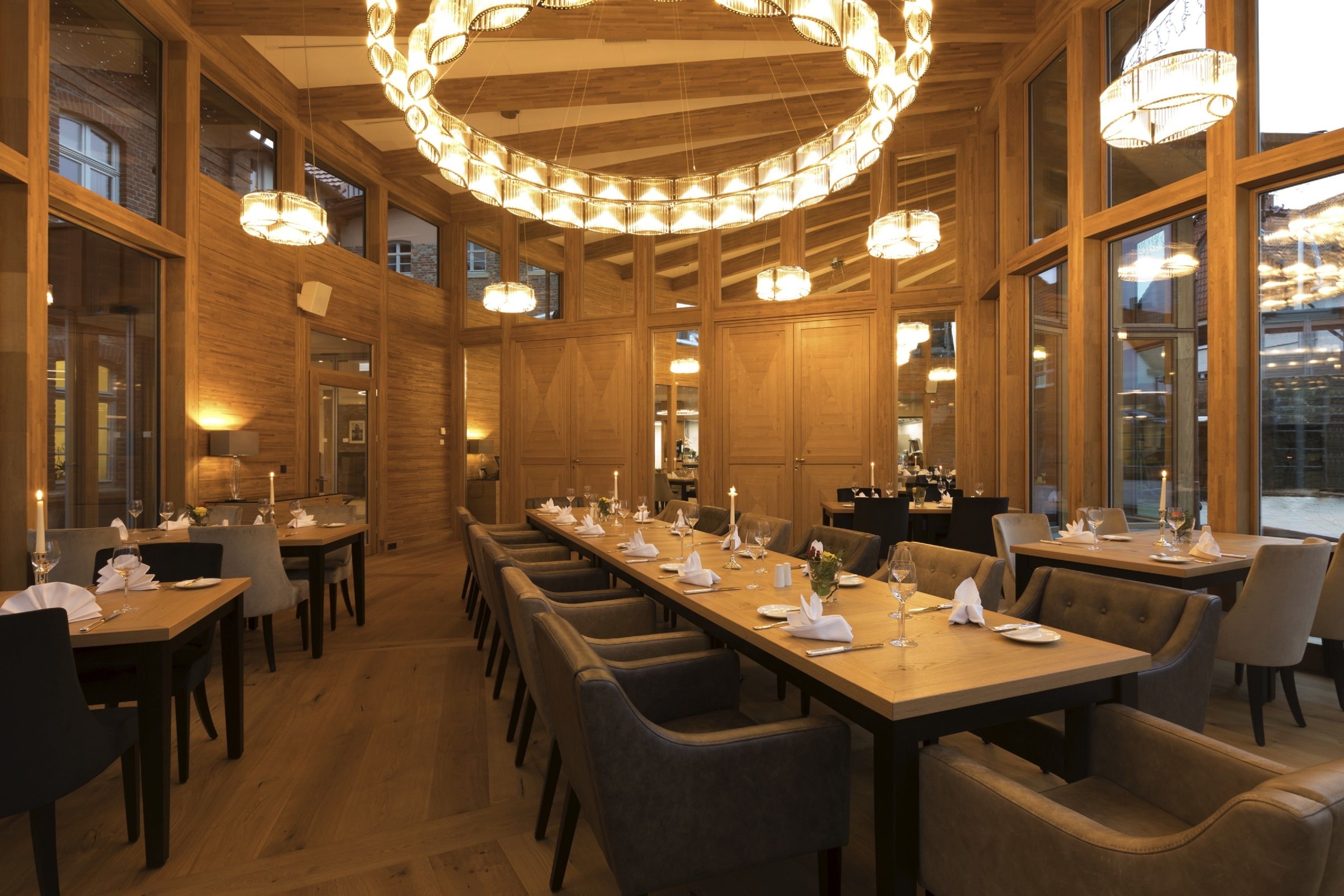 Un comedor amplio con mesas largas, varios candelabros y ventanas grandes.