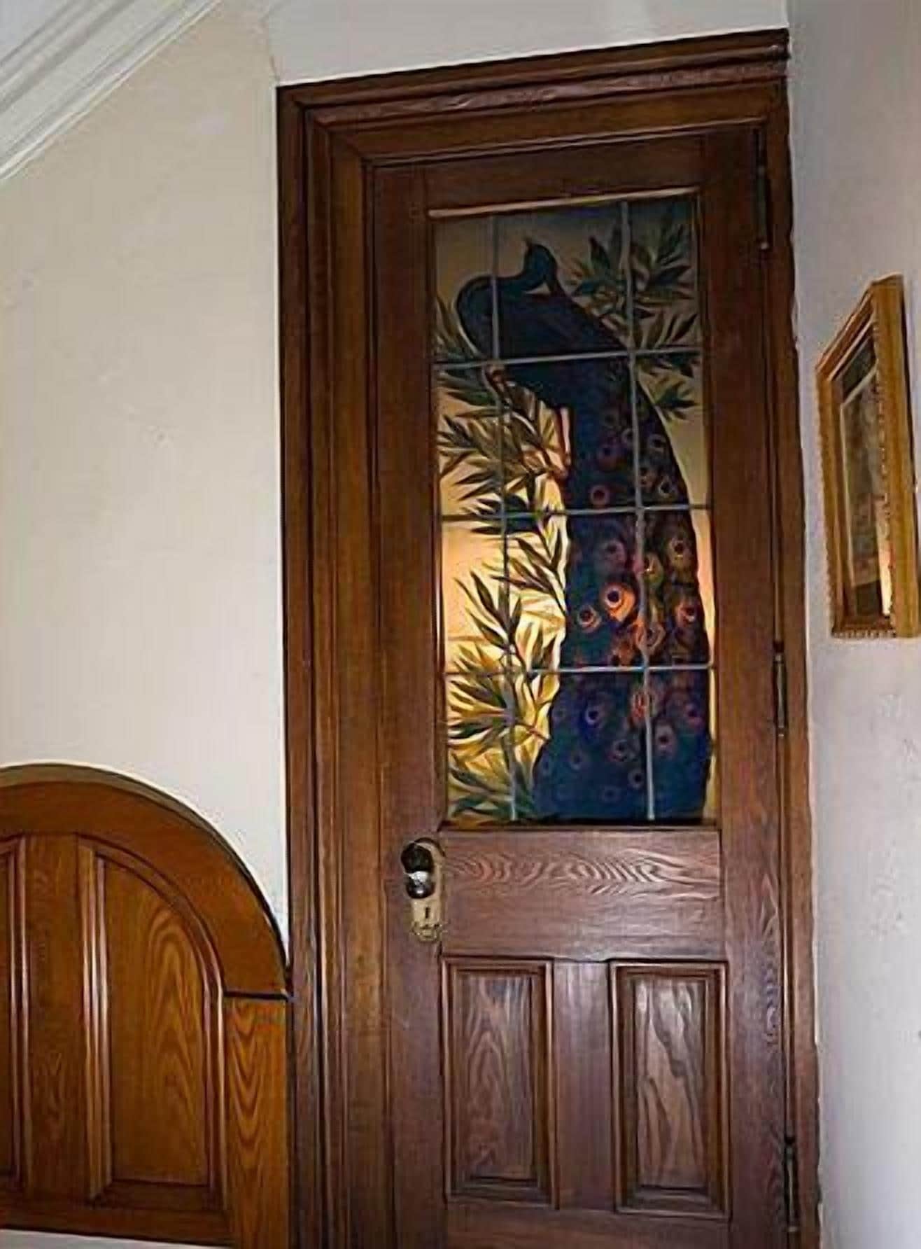 A wooden door with a glass panel featuring a peacock design.
