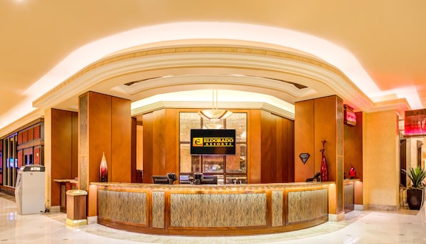 Un área de recepción con un mostrador curvo de madera, un cartel de Eldorado Resorts y una lámpara de araña moderna.