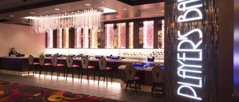 A bar area with a neon sign, bar counter, chairs, and a decorative light fixture.