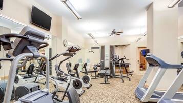Une salle de sport équipée de divers appareils d’exercice, notamment des tapis de course et des vélos elliptiques, et dotée d’un téléviseur fixé au mur.
