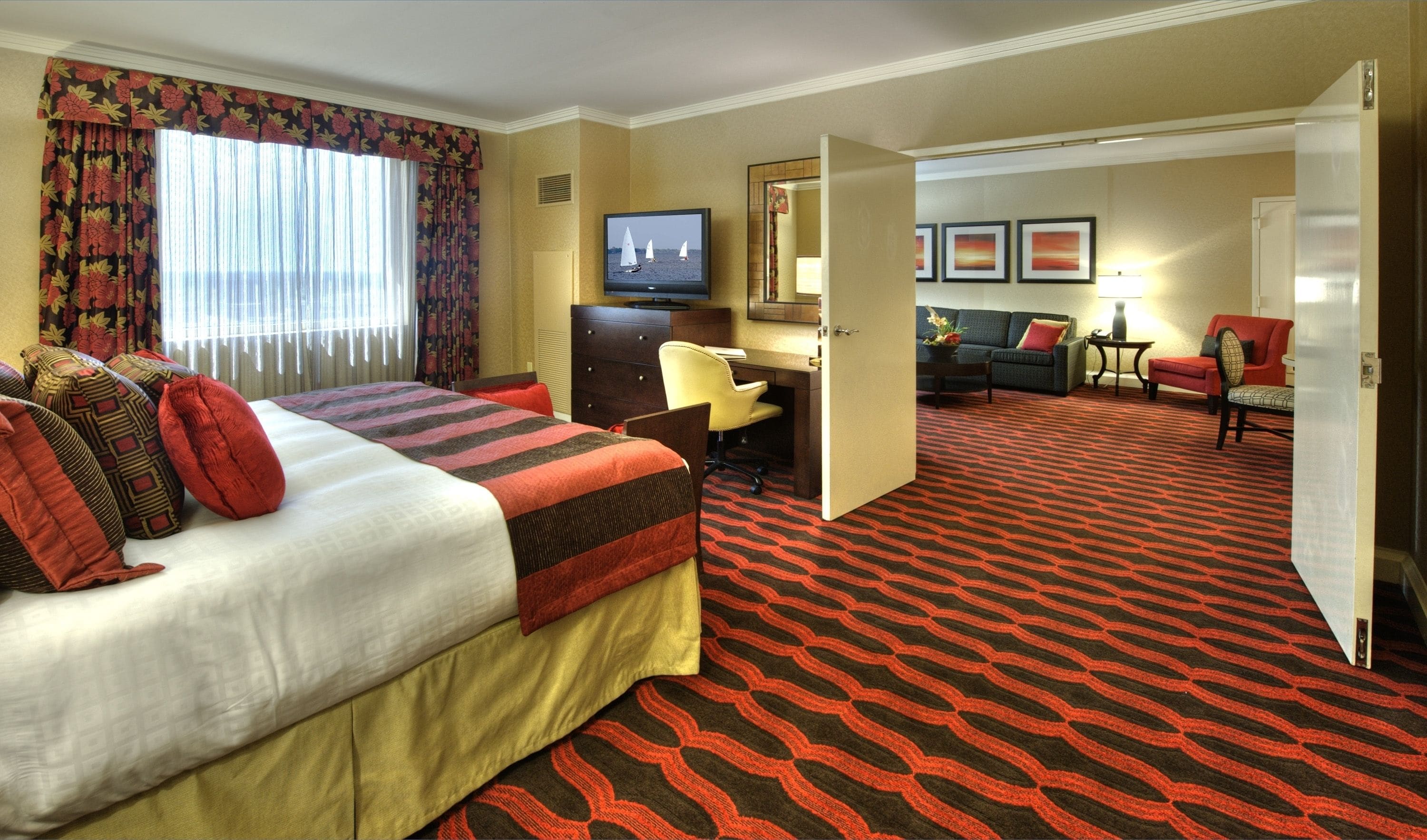Una habitación de hotel con cama, escritorio, televisión, sofá y alfombra estampada.