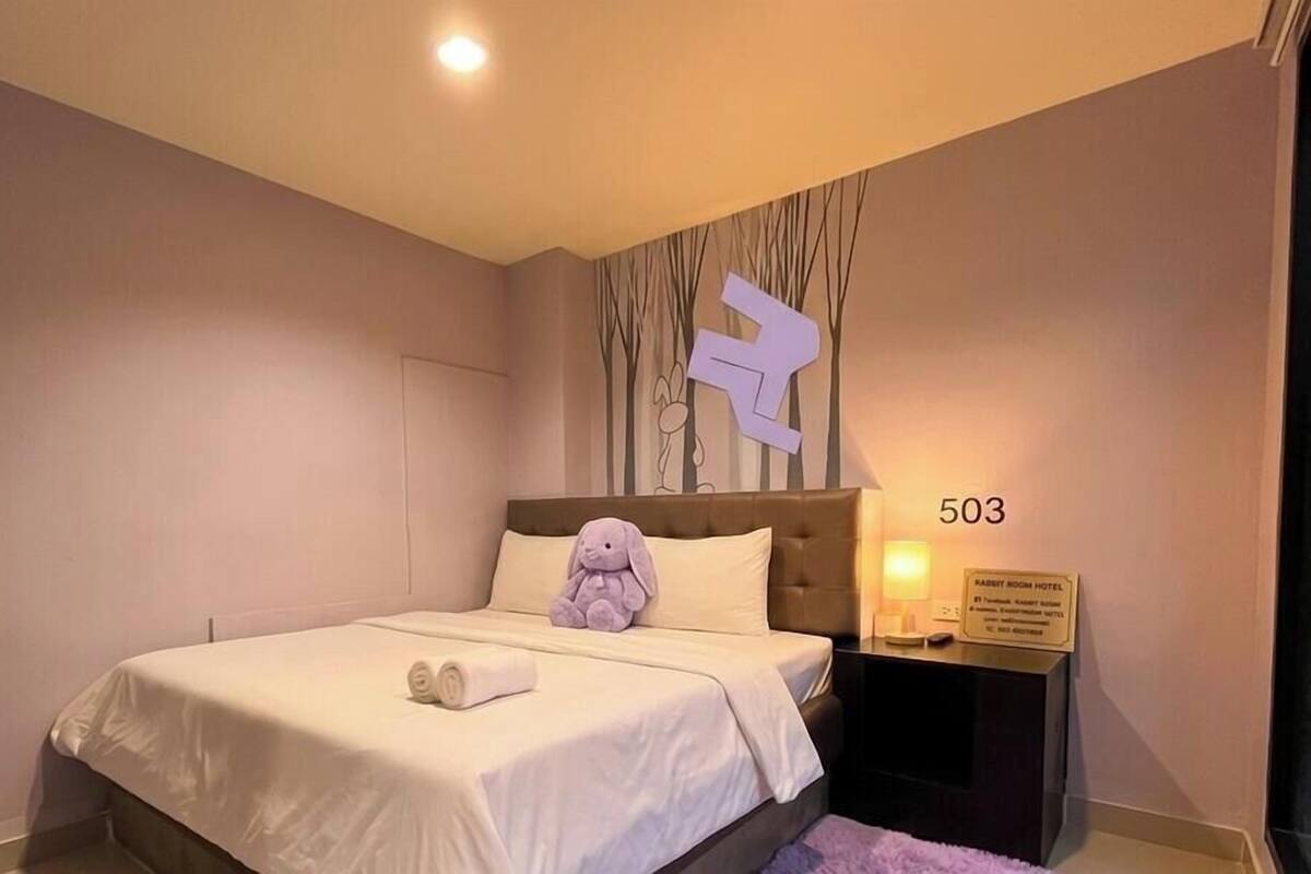 A hotel room with a bed, a plush toy, a nightstand, and a sign indicating the room number 503.