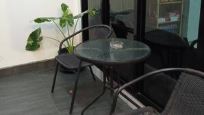 A glass-walled balcony with a round table and chairs, a potted plant, and a vending machine.
