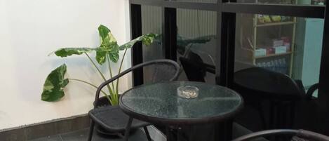 A glass-walled balcony with a round table and chairs, a potted plant, and a vending machine.