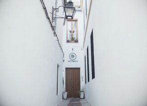 A narrow alleyway with a wooden door, a hanging lantern, and a building with a sign reading "LOFTTRIGO13". - Lofts Trigo 13 (Córdoba)