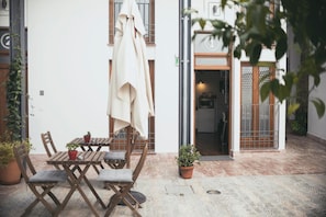 An outdoor seating area with wooden tables and chairs, a beige umbrella, and potted plants. - Lofts Trigo 13 (Córdoba)