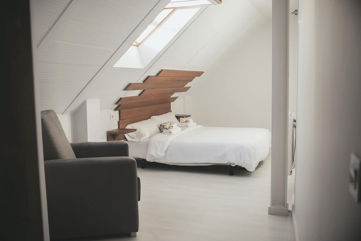 Ein Schlafzimmer mit schrägen Wänden, einem Bett, einem Nachttisch und einem Sessel.