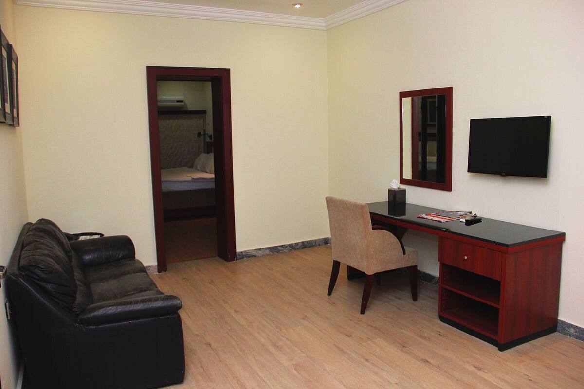 A room with a black leather sofa, a wooden desk with a chair, a television, and a mirror on the wall.