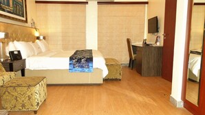 A hotel room with a bed, a desk, a chair, a TV, and a painting on the wall. - Capital Inn Plus (Ibadan)