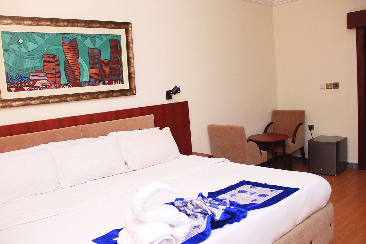 A hotel room with a large bed, a chair, a desk, and a painting on the wall.