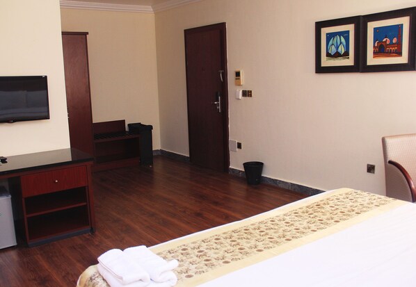 A hotel room with a bed, a desk, a chair, a television, and a door.
