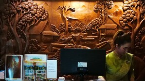 A reception desk with a wooden carved backdrop, a computer monitor, and informational brochures. - The Imperial Home Hotel (Bangkok)