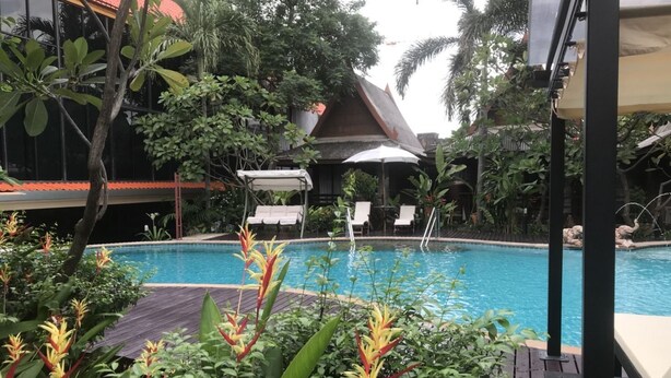 A pool area with a wooden deck, lounge chairs, and tropical plants. - The Imperial Home Hotel (Bangkok)