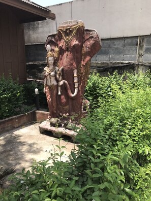A large elephant statue with a seated figure on its back, surrounded by greenery and a concrete structure in the background. - The Imperial Home Hotel (Bangkok)