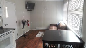 A compact living space with a kitchenette, a sofa, a table, a fan, and a TV.