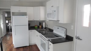 Una cocina compacta con alacenas blancas, un microondas integrado, estufa y refrigerador.